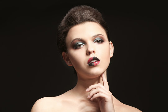 Beautiful young woman with creative makeup on dark background
