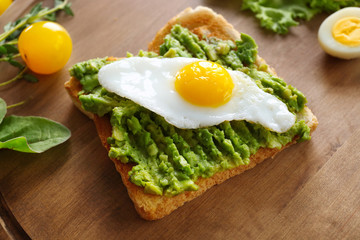 Tasty breakfast toast with avocado and quail egg on wooden board
