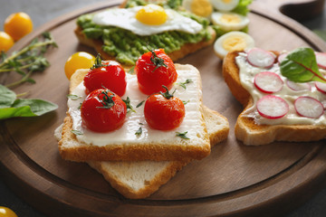 Different tasty breakfast toasts with vegetables on wooden board