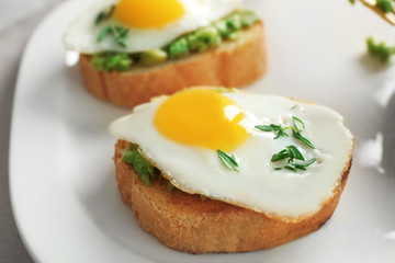 Tasty breakfast toasts with avocado and quail eggs on plate, closeup