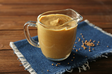 Glass jug with delicious mustard sauce on wooden table