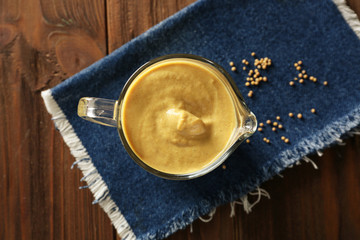 Glass jug with delicious mustard sauce on wooden table