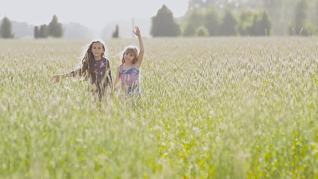 Two sisters with long curly hair running around the field with wheat on a warm sunny day