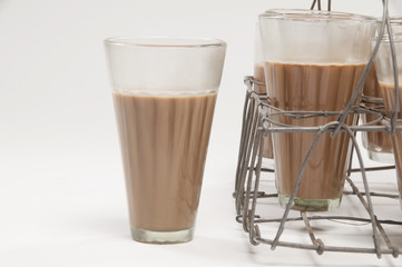 Glass of chai kept besides grid tray over white background 