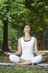 Fototapeta na wymiar Young woman in lotus position meditating in a park 