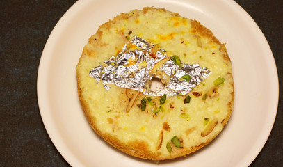 Indian disc-shaped mithai, ghevar sweet garnished with dry fruits and silver leaf.