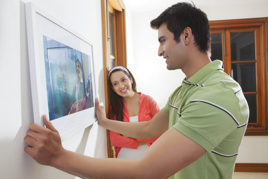 Young man hanging a picture on the wall while young woman looks
