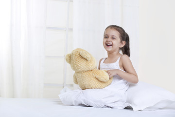 Girl laughing while playing with teddy bear 