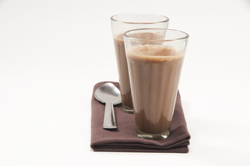 Glasses of chai and steel spoon kept on table napkin isolated over white background 
