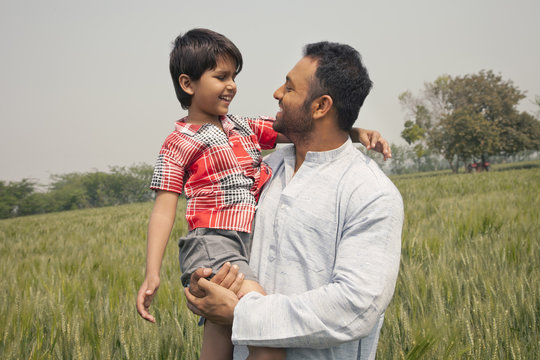 Happy father and son looking at each other with wheat field in background 