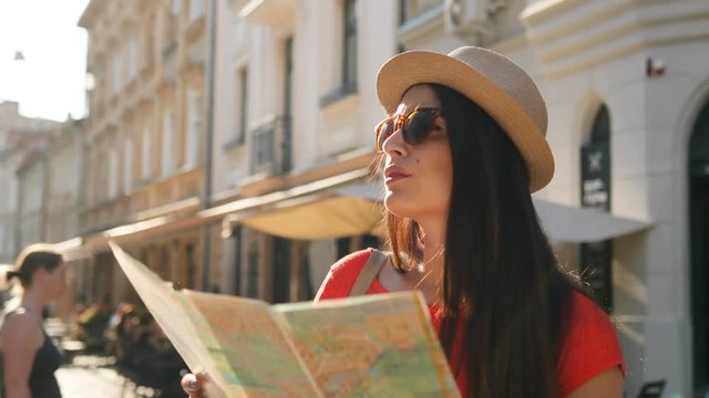 Young attractive woman tourist in sunglasses walking the street with paper map and searching right street, place. Woman sightseeing in the old city.