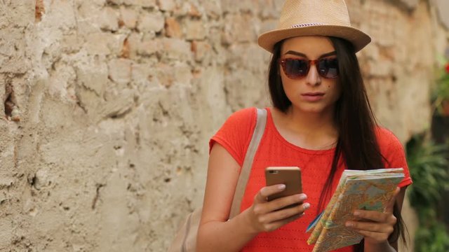Young attractive woman sightseeing in the old city. Female traveler using paper map and online maps on smartphone to find interesting places. Close up