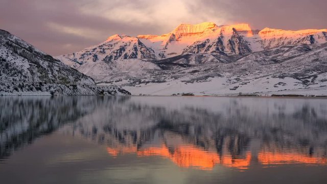 Sun lighting up snow covered mountain reflecting over Deer Creek Reservoir Utah.