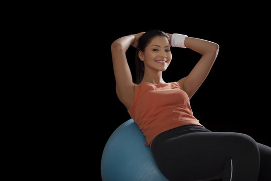 Portrait of a young woman doing abdominal exercise on a fitness ball over black background 