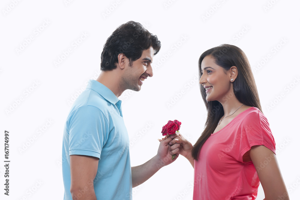 Wall mural side view of happy man giving rose to woman over white background