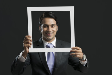 Portrait of happy businessman holding picture frame over black background