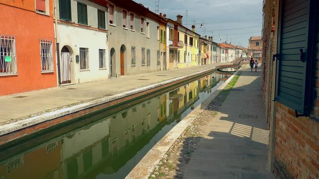 pidgeon flying over water canal in lagoon town, colorful houses and buildings lining, color graded clip