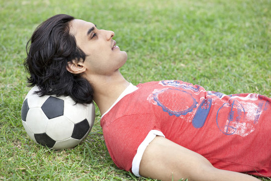 Handsome young man lying on back with head on soccer ball 
