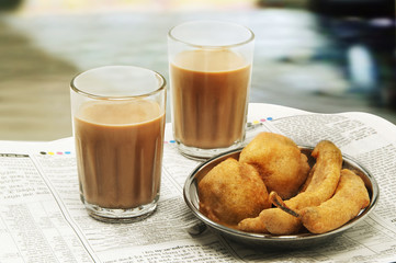 Close-up of morning chai with bhajiyas and fried potato balls on newspaper 