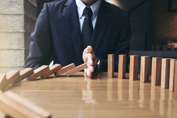 Close up of businessman hand Stopping Falling wooden Dominoes effect from continuous toppled or...