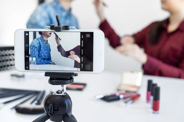 Happy smiling elegant woman or beauty blogger with brush on recording video while review product make up tutorial for theme about video blogging on camera screen