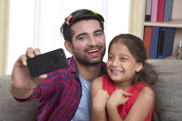 Father wearing make-up having fun with daughter taking selfie