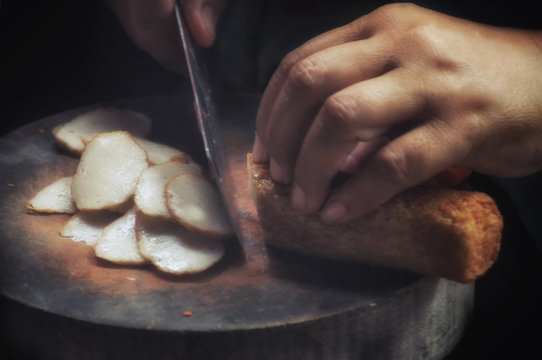 Chef using knife to slice chinese fish cake on wooden chopping board at street market