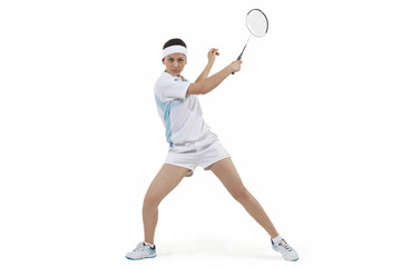 Young woman in sports wear playing badminton against white background