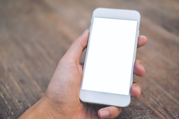 Mockup image of hand holding white mobile phone with blank screen on vintage wood table in cafe