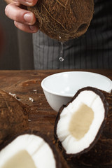 Fresh coconut water pouring into white bowl on wooden table. Healthy and natural product from exotic fruits ingredients