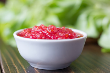 Mexican salsa or indian chutney in white ceramic bowl against green herbs