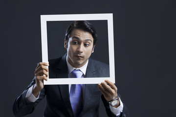 Businessman looking down while holding picture frame against black background