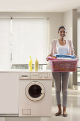 Young woman standing near washing machine with laundry basket