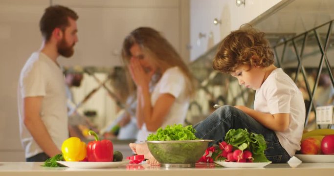The background of the emotional quarreling parents fighting behind the little charming boy playing in the mobile phone. The mother is slapping her husdand.