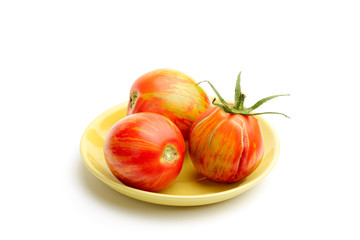 Three juicy red zebra tomatoes in a little yellow porcelain plate, isolated on white background