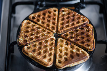 Macro shot of just cooked, delicious, tasty, hot yogurt pancakes with strawberry sauce on waffle iron on fire stove in kitchen. Dinner is ready. Sweet golden brown waffles with jam ready to be eaten