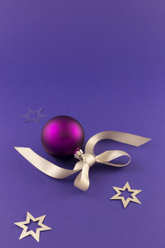 Beautiful purple christmas ball with satin effect, grey gift ribbon and metallic silver stars on purple background.