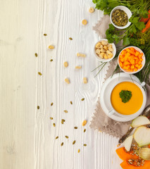 Pumpkin cream soup with croutons, raw fresh pumpkin pieces  and herbs on a white rustic wooden background