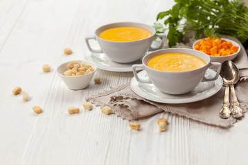 Pumpkin cream soup with croutons, raw fresh pumpkin pieces  and herbs on a white rustic wooden background