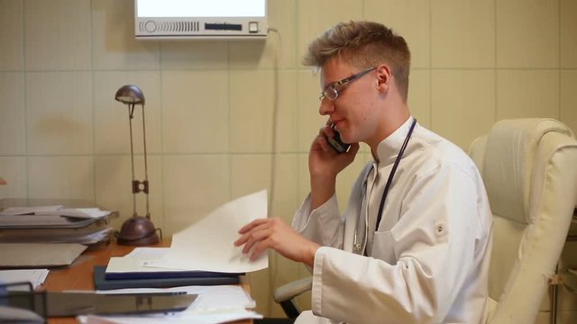 Doctor looks happy while speaking on cellphone and checking documents
