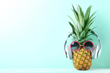 Ripe pineapple with sunglasses and headphones on mint background