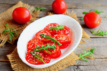 Salad with tomato, rucola, sesame seeds and vinaigrette dressing. Quick tomato salad on a white plate and an old wooden table. Healthy recipe for breakfast, lunch and dinner. Rustic style