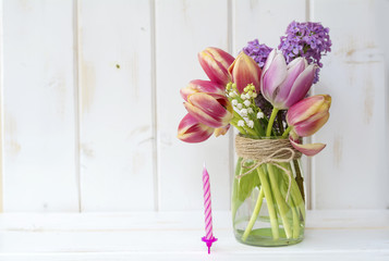 bouquet of tulips and lilac with birthday candles  on a white wooden background