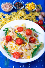 Pasta salad with tomatoes cherry, tuna, corn and arugula. Top view.