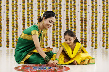 Mother and daughter placing diyas on a rangoli 