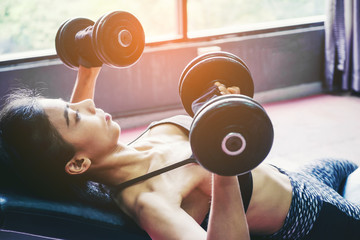 Asian sports woman doing exercises with dumbbell weights in gym