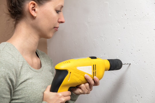 Frau bohrt mit der Bohrmaschine ein Loch in die Wand