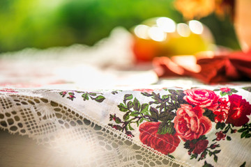 Golden autumn. Macro shot of natural linen tablecloth with rose print and crochet white lace trim, yellow apples and a vase, full of vibrant maple leaves on top of rustic table on colorful background