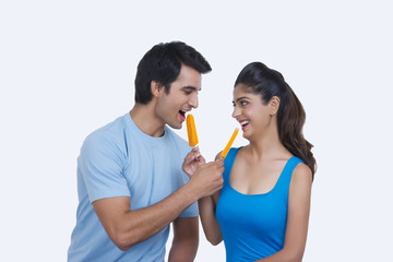 Loving young couple feeding each other ice lollies over white background