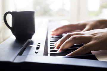 A woman playing piano at the window. A cup of coffee is on the instrument